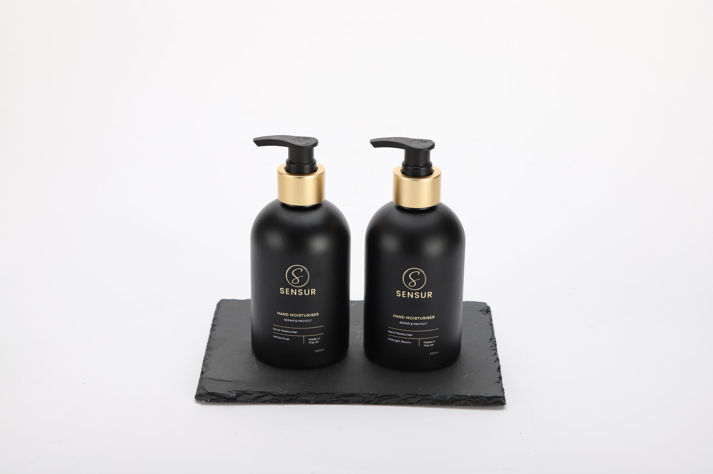 Two black bottles with gold caps on a black tray against a white background