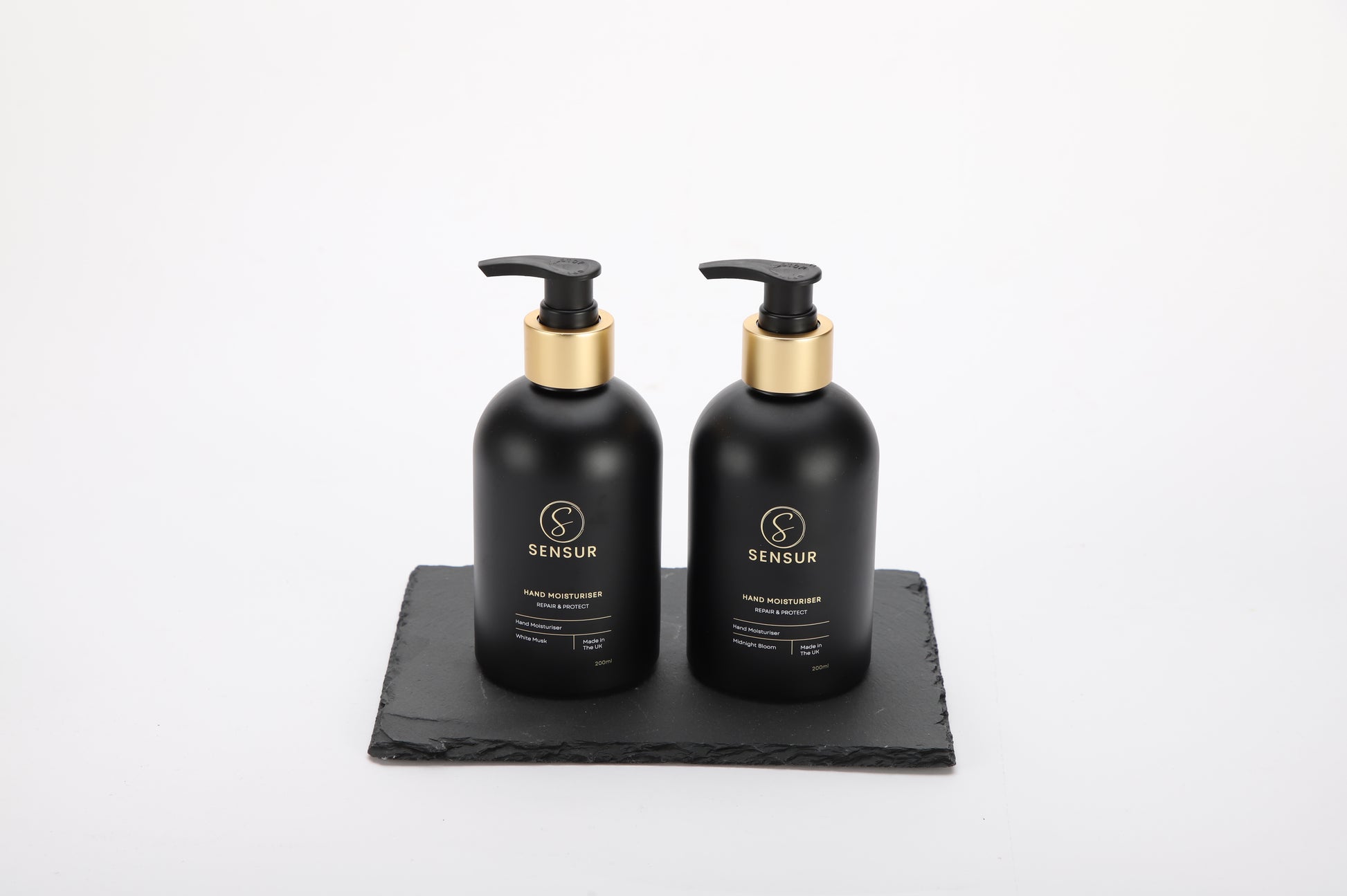 Two black bottles with gold caps on a black tray against a white background