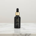 Black dropper bottle with gold cap on a marble surface against a dark background
